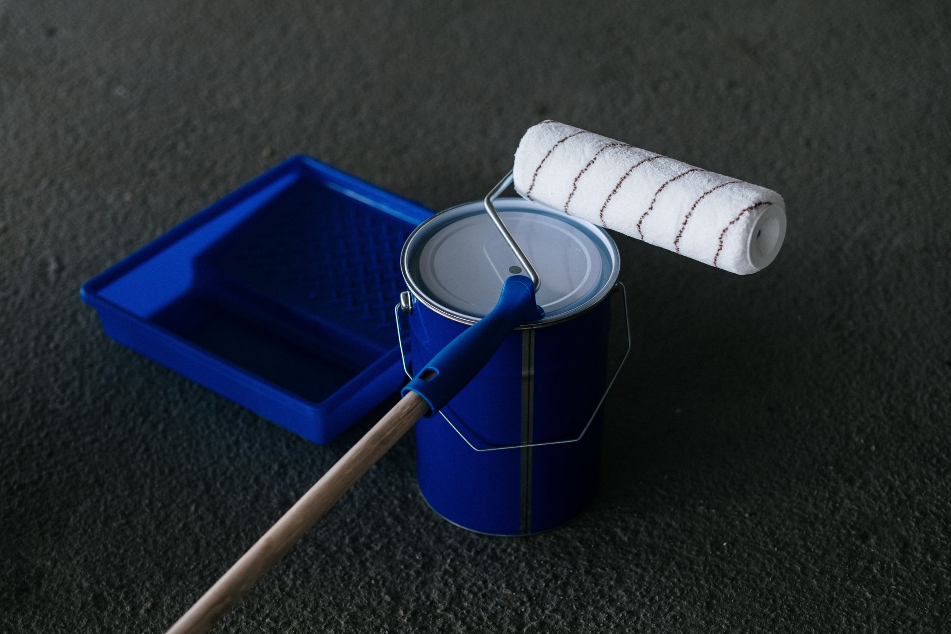 Close-up of a paint can, roller, and tray on a textured floor in Long Beach, CA